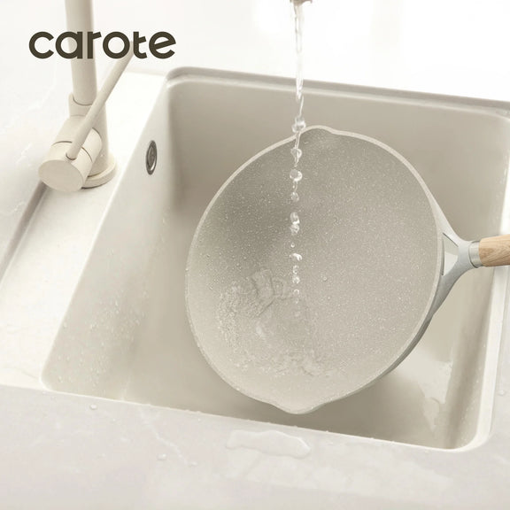 Spatula with wooden handle being rinsed under running water in a sink, branded 'carote'.