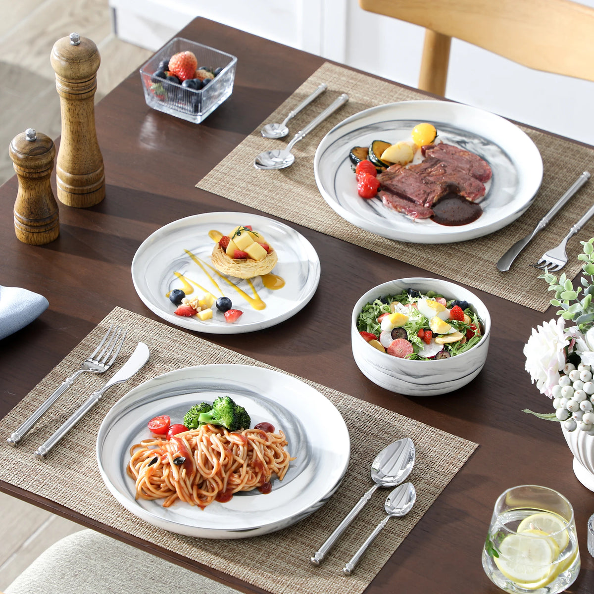 Dining table set with plates of food including spaghetti, salad, and a steak, along with cutlery and glasses.