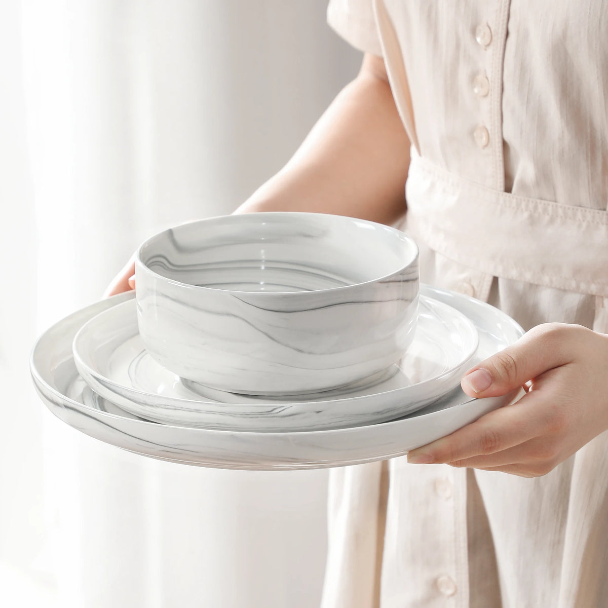Person holding a set of marbled ceramic plates and bowls.