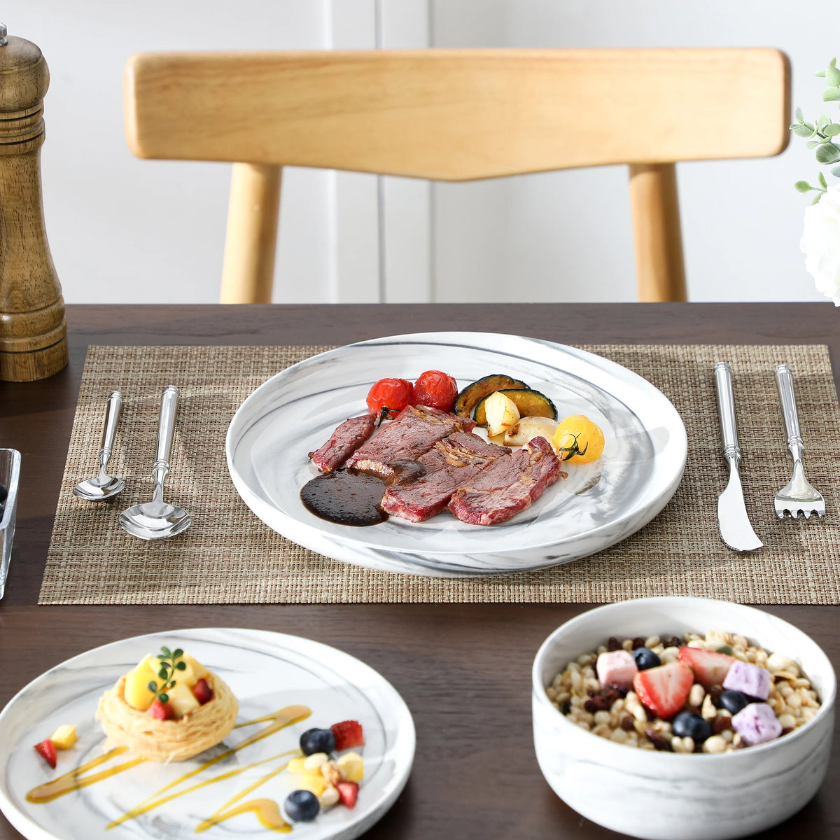 Dinner table setting with plates of food and cutlery on a wooden chair.