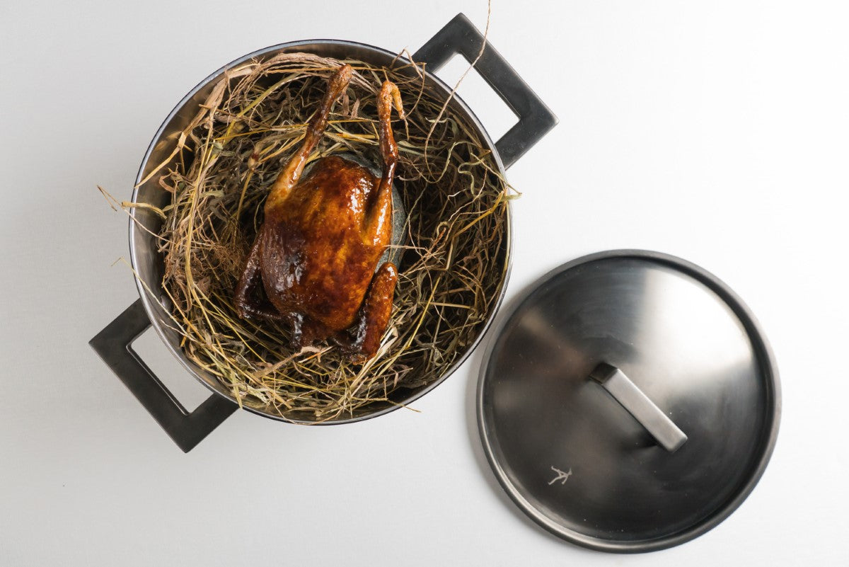 Roasted duck in a pot with a lid on a white background