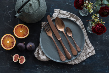 Table setting with gray plates, cutlery, and fruit on a dark surface.