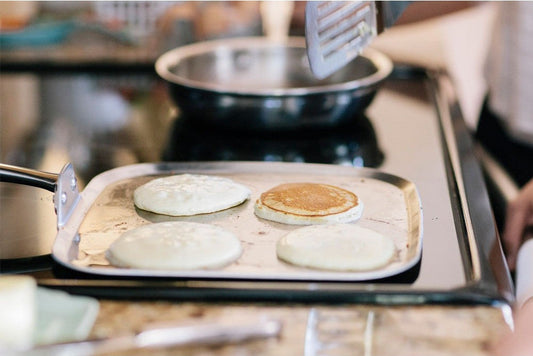 Pancakes being flipped on a griddle with a spatula.