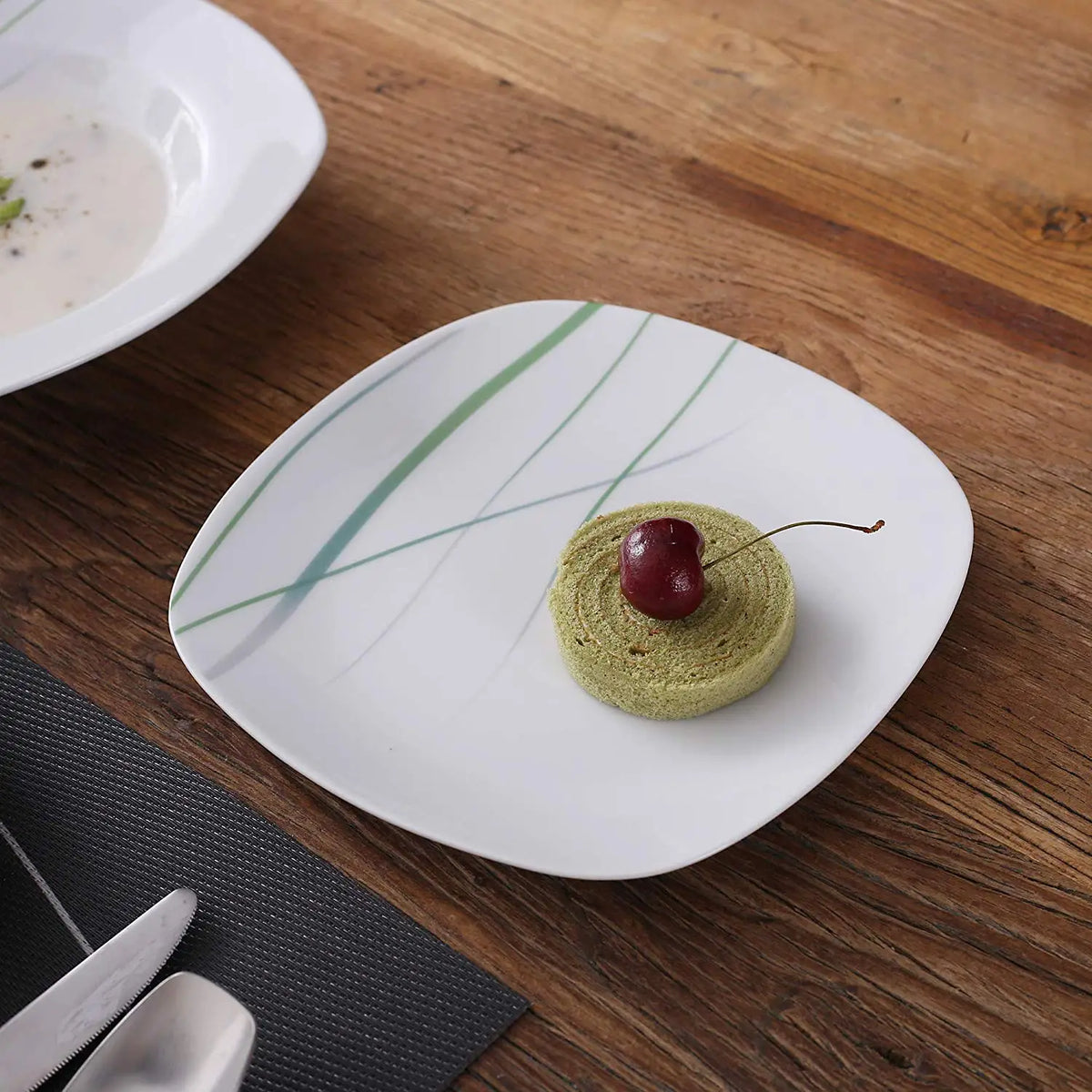 Green dessert on a white plate with a cherry on a wooden table