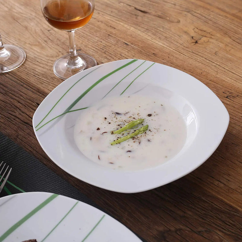 White bowl with creamy dish and green garnish on a wooden table with a glass of amber liquid.