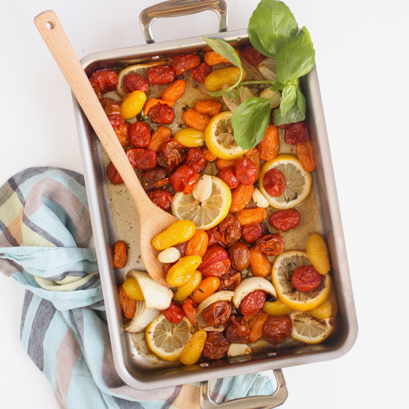 Roasted vegetables with lemon and herbs in a baking dish with a wooden spoon.