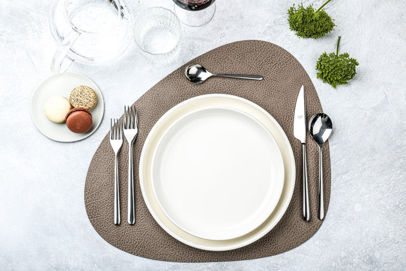 Dining table setting with white plates, silverware, and a textured placemat on a light gray surface.