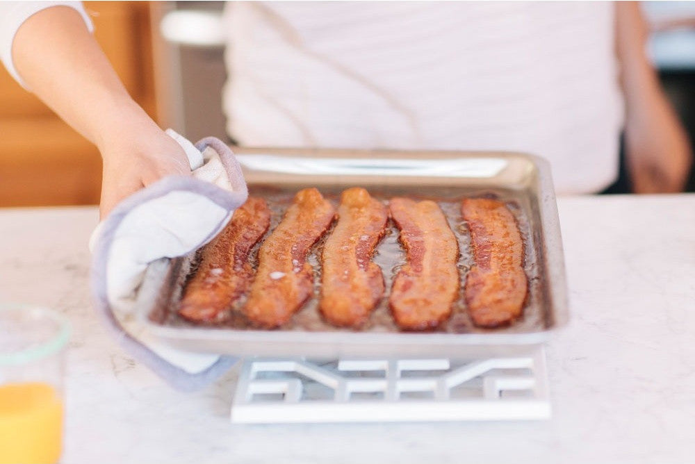 Person holding a tray with sausages on a kitchen counter
