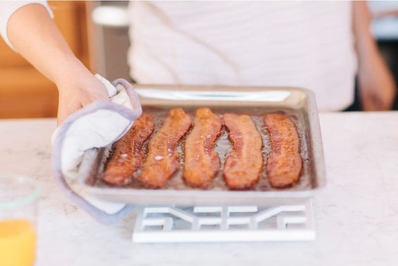 Person holding a tray with sausages on a kitchen counter