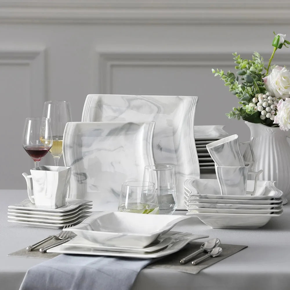 White marble dinnerware set on a table with glasses and flowers.
