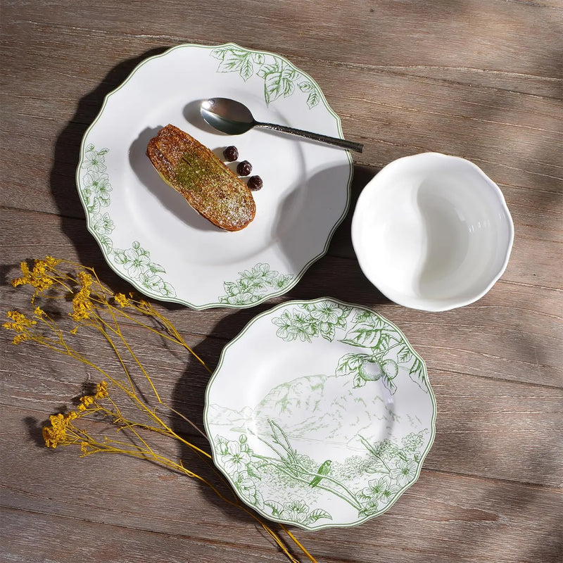White ceramic plates with green floral patterns on a wooden surface, accompanied by a small bowl and a piece of bread.