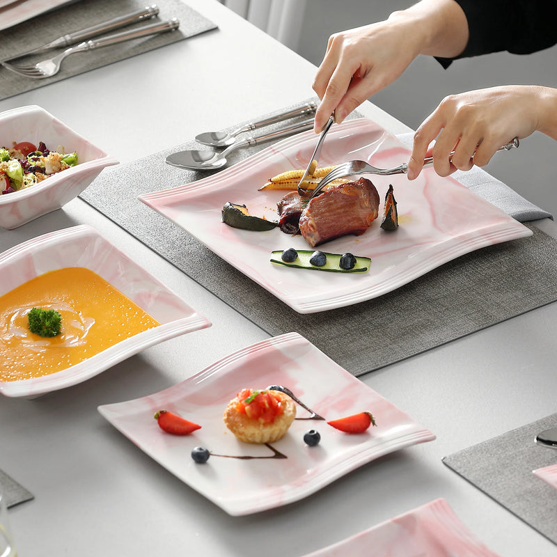 Person setting a table with plates of food and utensils on a gray surface.
