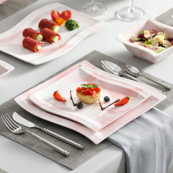 Dinner table setting with pink plates, silverware, and small desserts.