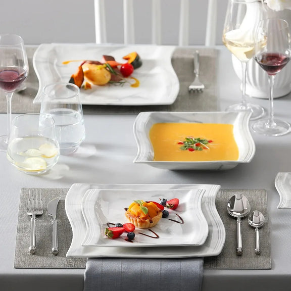 Elegant dining table setting with plates, glasses, and cutlery on a gray surface.