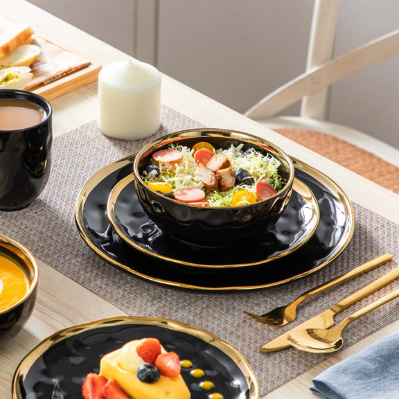 Dining table setting with black and gold plates, salad, and coffee.
