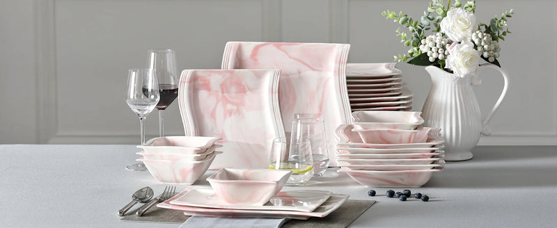 Pink marble-patterned dinnerware set on a table with glasses and a vase.
