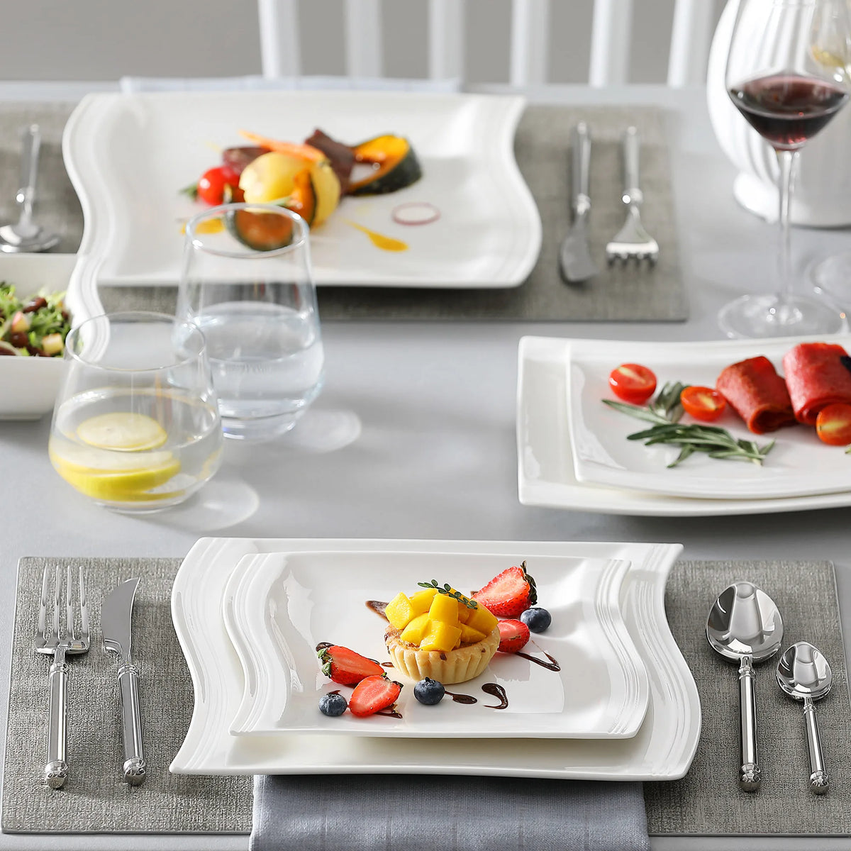 Dining table set with plates of food, glasses, and cutlery on a gray tablecloth.