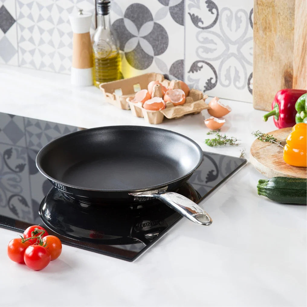 Black frying pan on a stove with vegetables on a kitchen counter
