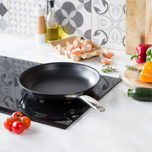 Black frying pan on a stove with vegetables on a kitchen counter