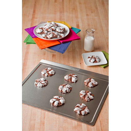 Baking sheet with cookies on a wooden surface, surrounded by colorful napkins and a glass of milk.