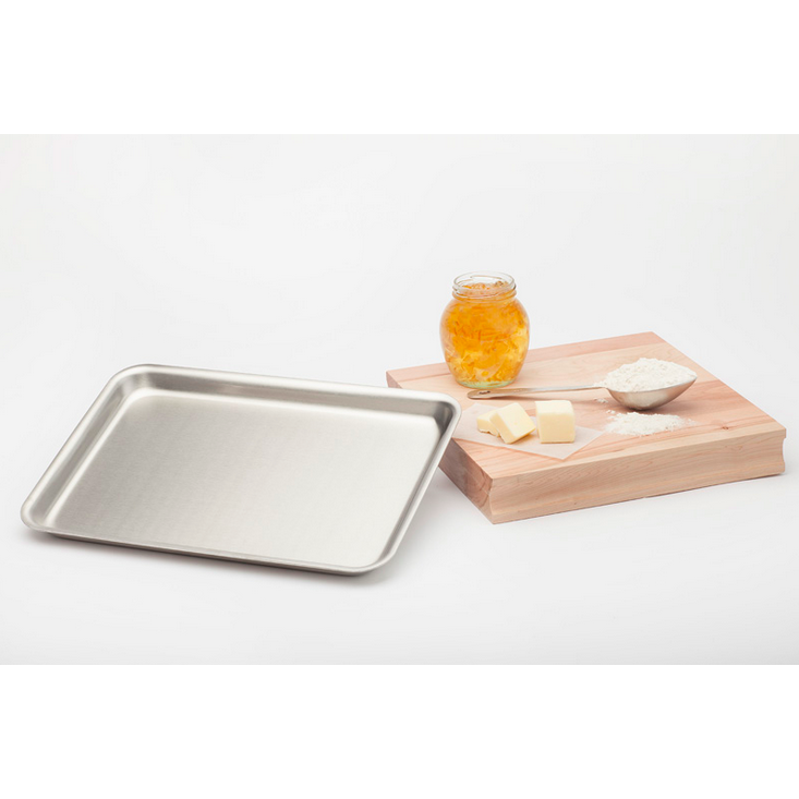 Metal baking tray on a white background with a wooden cutting board featuring honey, butter, and flour.