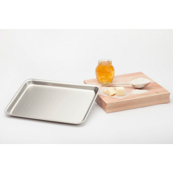 Metal baking tray on a white background with a wooden cutting board featuring honey, butter, and flour.
