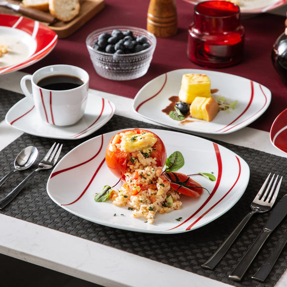 Dessert table setting with a dish of stuffed tomato, coffee, and fruit on a red and white tablecloth.