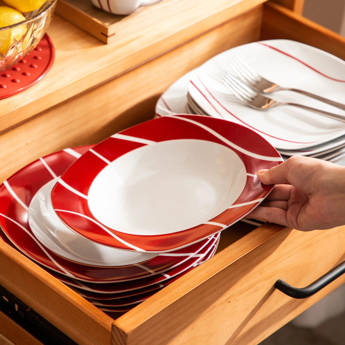 Red and white striped plates being taken out of a wooden drawer.