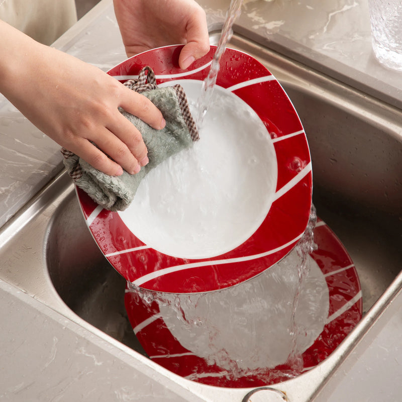 Person washing a red and white dish in a sink with water and soap.