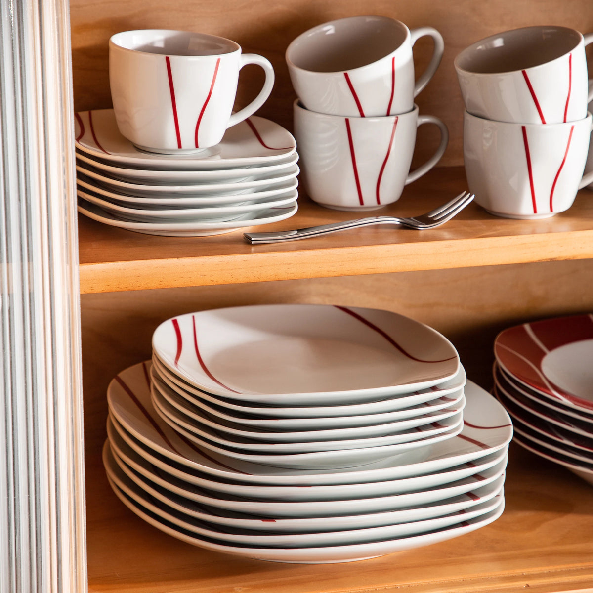 Dishware set with white cups and plates featuring red stripes on a wooden shelf.