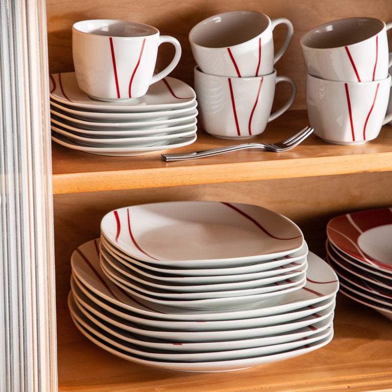 Dishware set with white cups and plates featuring red stripes on a wooden shelf.