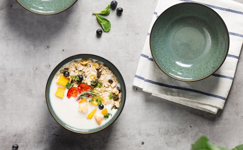 Bowl of oatmeal with fruits and nuts on a gray surface with a green plate and striped towel.