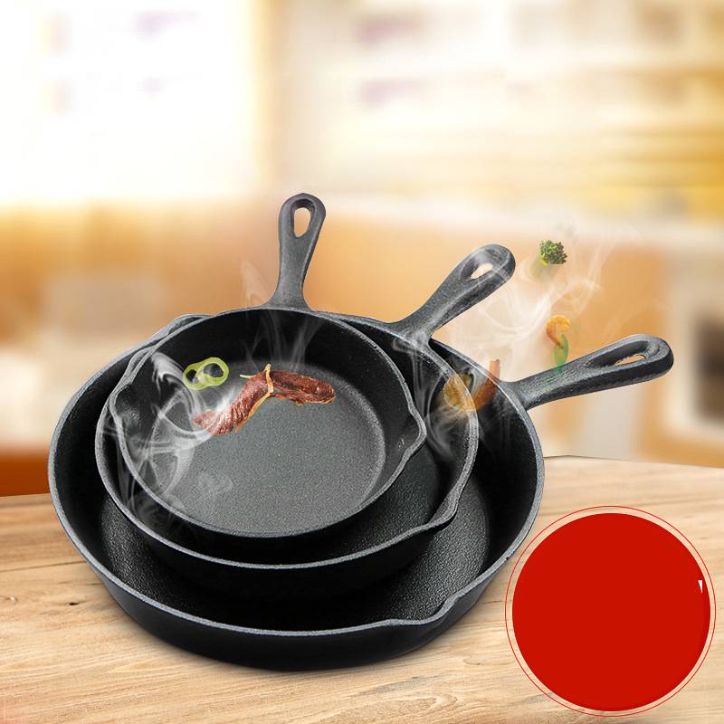Set of three cast iron skillets on a wooden surface with a blurred kitchen background.