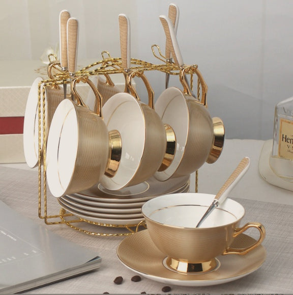 Set of gold and white tea cups and saucers with a stand on a table.