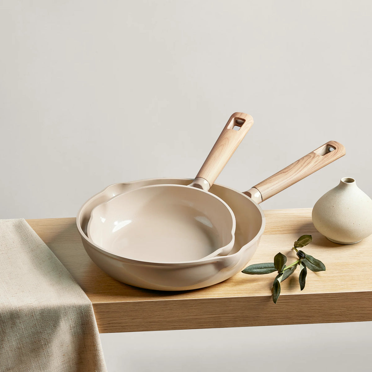 Beige ceramic cookware set on a wooden surface with a light background