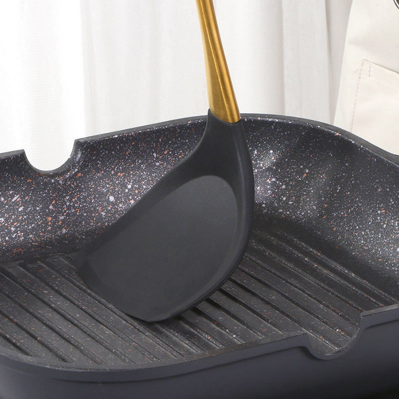 Black speckled grill pan with a black spatula on a white background