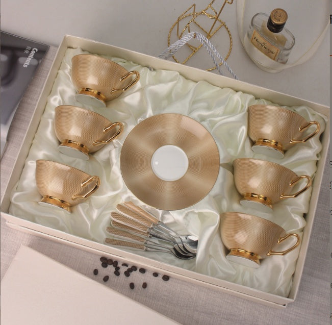 Set of gold ceramic tea cups and saucers in a decorative box with silver spoons.