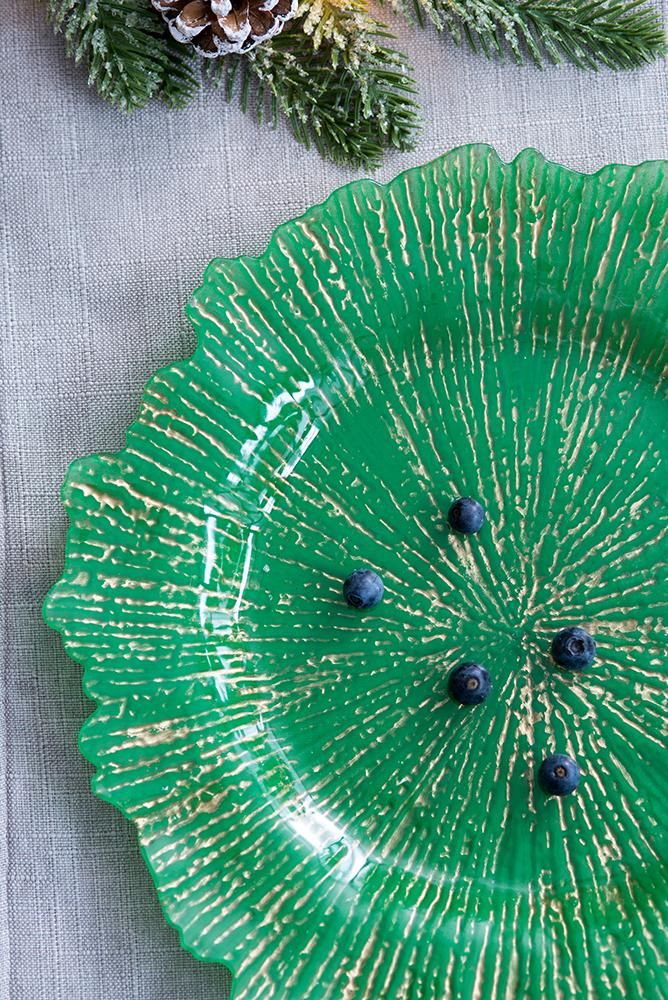 Green glass charger plate with textured design on a light gray surface with pine branches.