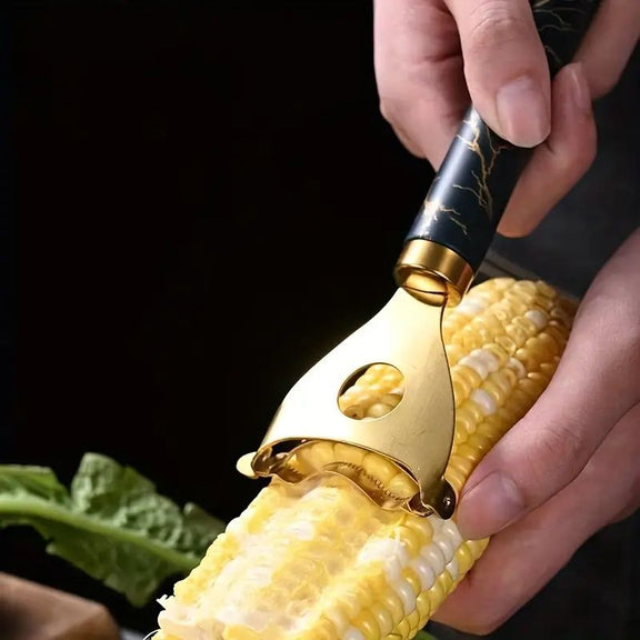 Corn shucker with gold blade being used on a corn cob against a black background