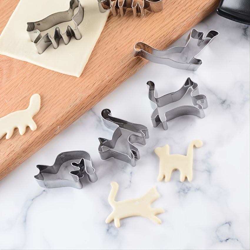 Set of cat-shaped cookie cutters on a marble surface with some cut-out cookies.