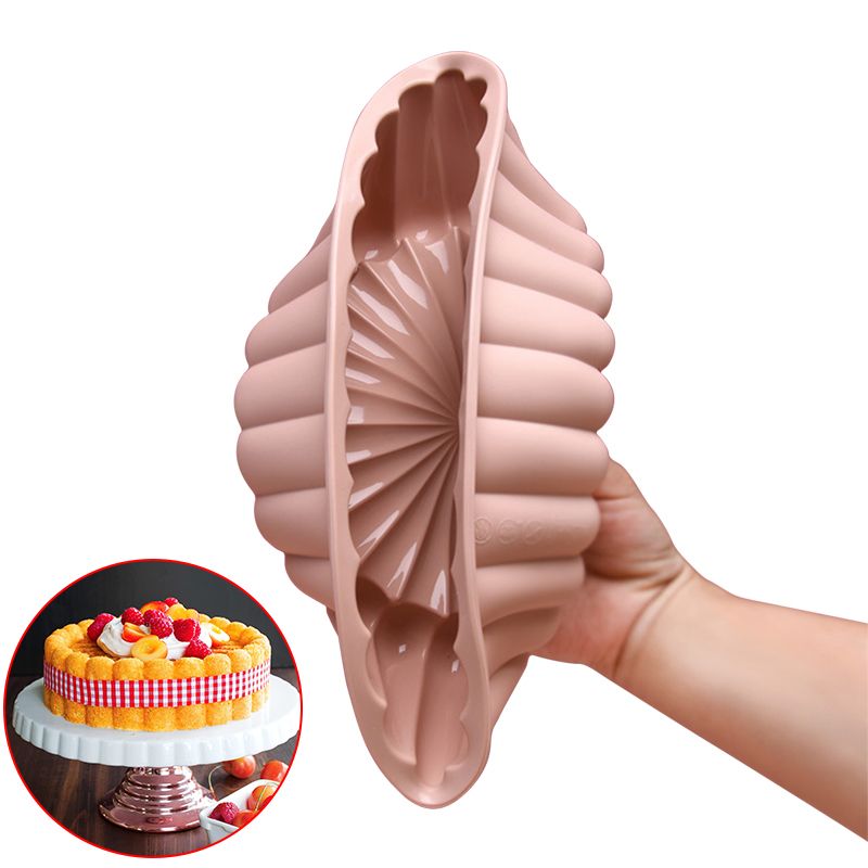 Silicone mold shaped like a shell held by a hand, with a cake in the background.