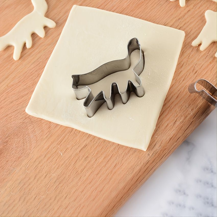 Metal reindeer cookie cutter on a square of dough with wooden surface and marble countertop in the background.