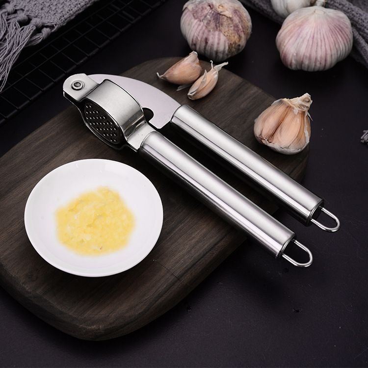Garlic press with mashed garlic on a wooden board