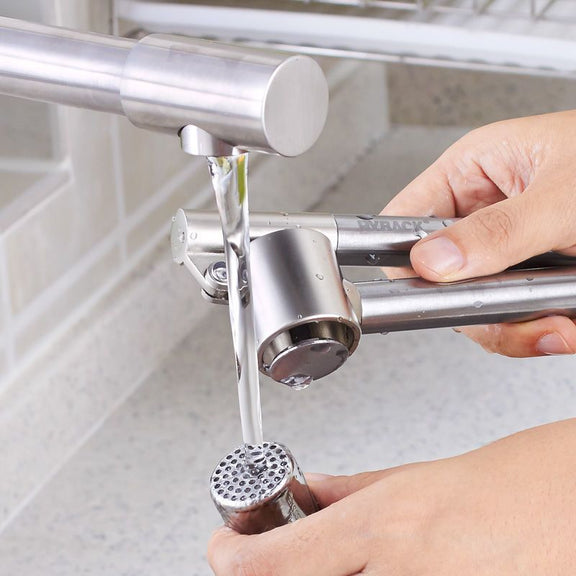 Person using a manual garlic press to crush garlic over a sink.