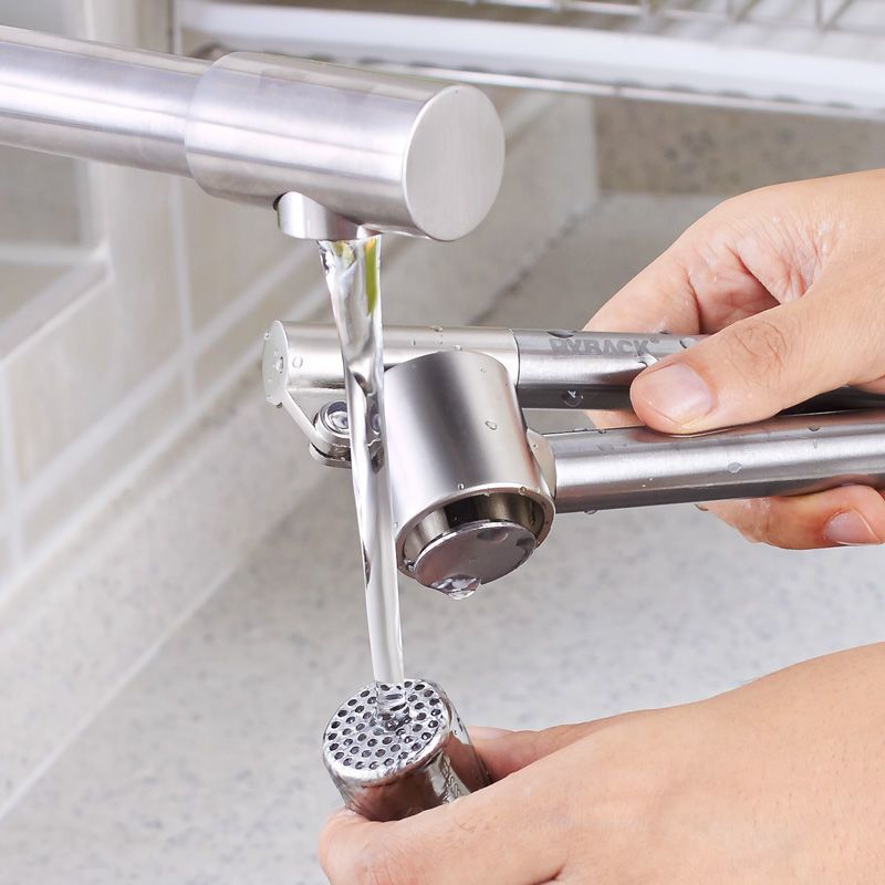 Person using a manual garlic press to crush garlic over a sink.