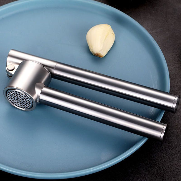 Stainless steel garlic press on a blue plate with a clove of garlic