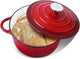 Red enameled cast iron Dutch oven with a lid containing bread on a white background