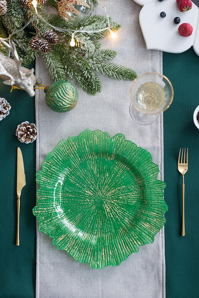 Green decorative glass charger plate on a festive table setting with Christmas decor.