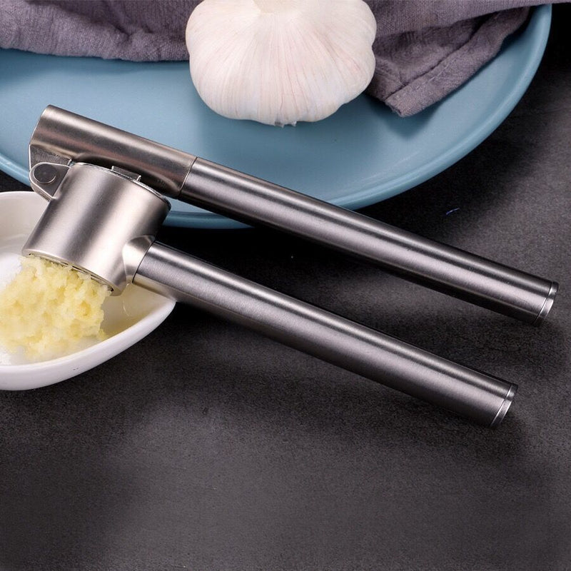 Stainless steel garlic press with minced garlic on a dark surface
