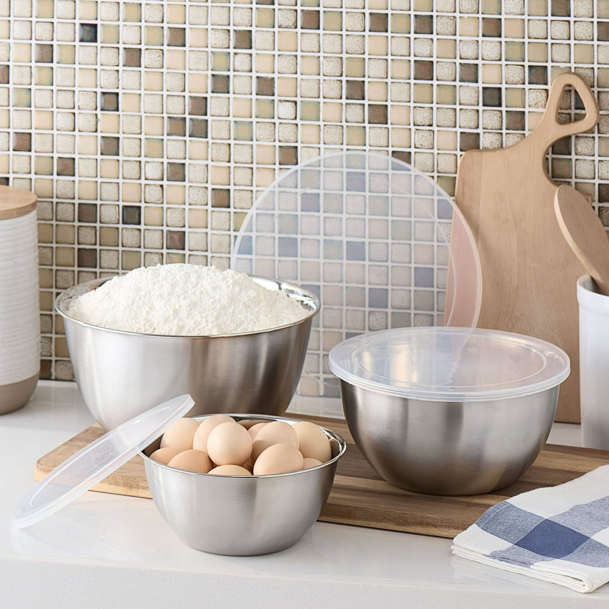 Metal mixing bowls with flour, eggs, and a tiled backsplash in a kitchen setting.